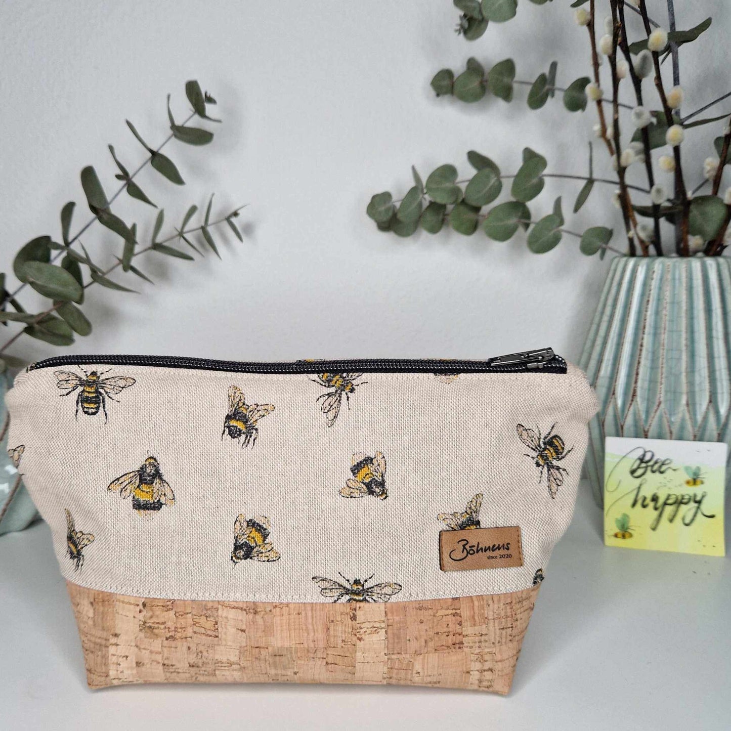 Necessaire "Biene" aus Canvas und portugiesischem Kork mit Bienenmuster, auf Tisch mit grünen Pflanzen im Hintergrund.