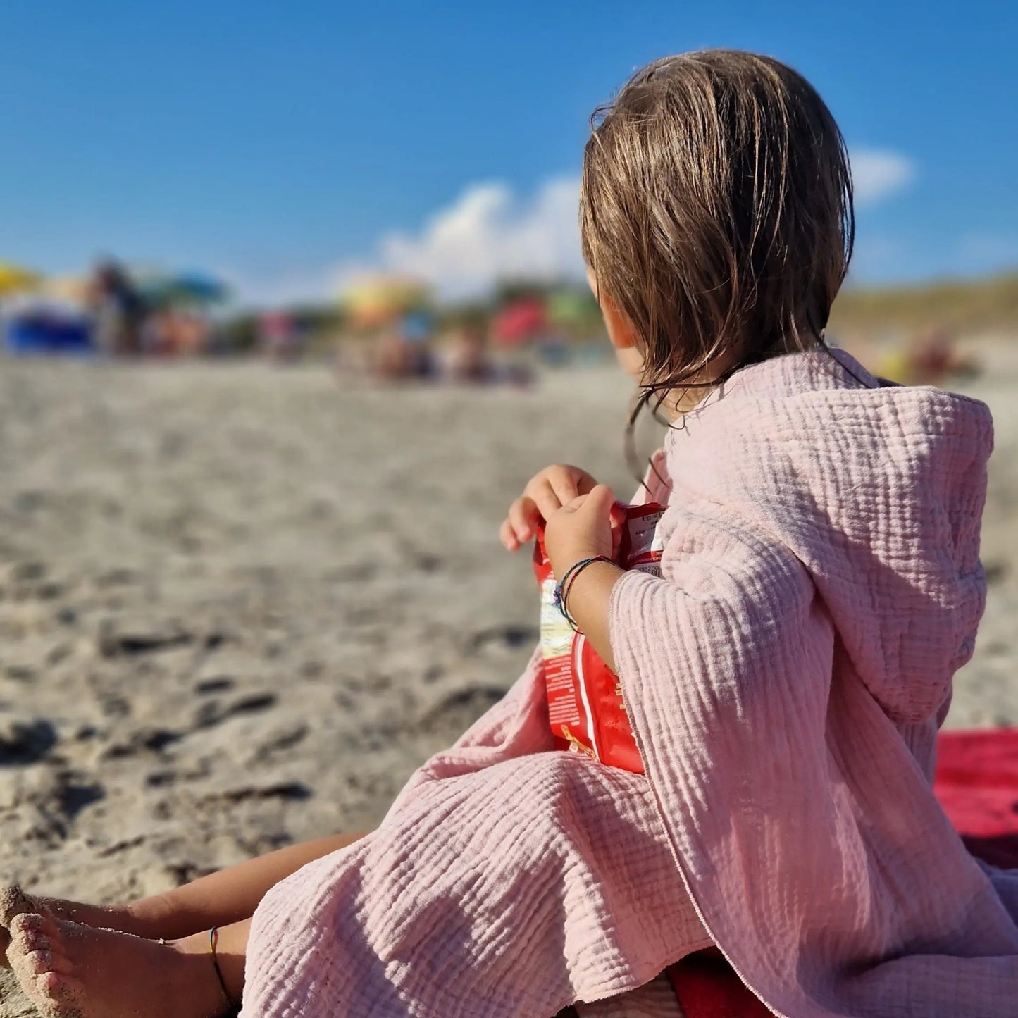 Child wearing pink muslin bath poncho on beach.
