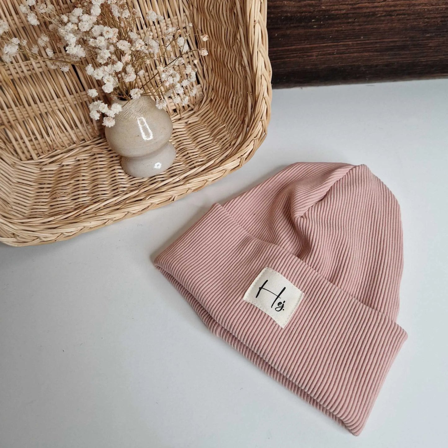 Kids pink hipster beanie, size 42, next to a wicker basket with dried flowers, perfect for autumn and winter.