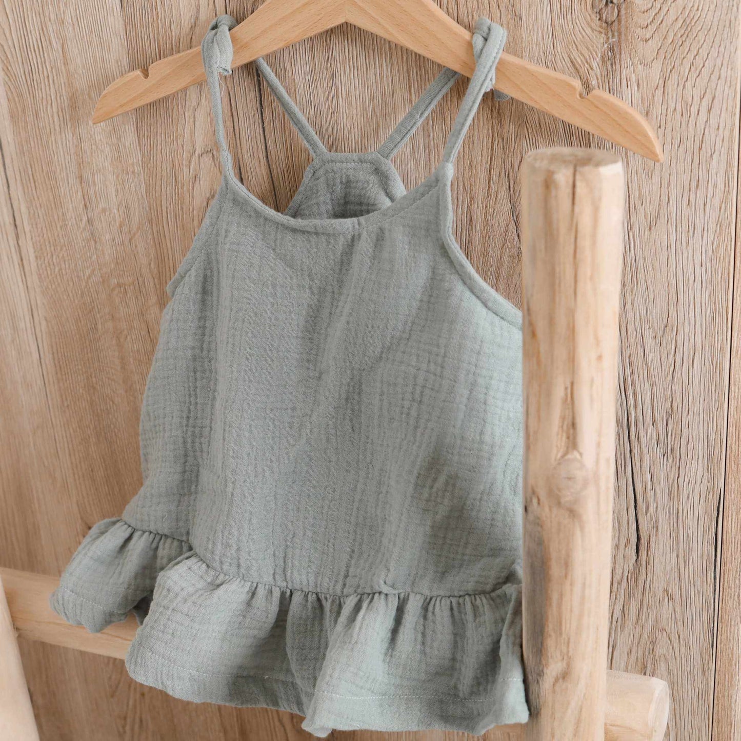 Musselin Trägertop altgrün mit Volant auf Holzkleiderbügel, ideales Sommerkleidungsstück für Mädchen.