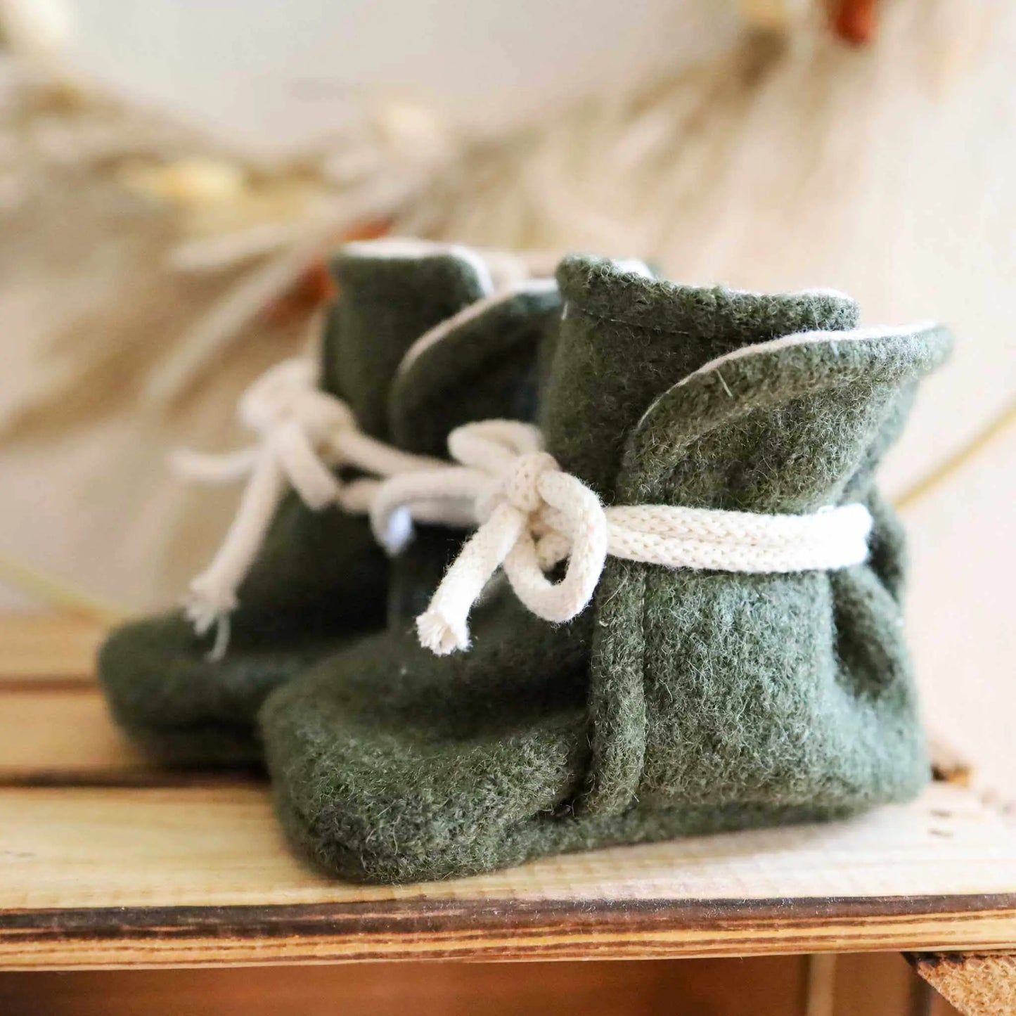 Babyschühchen aus Wollwalk in dunkelolive auf Holzboden.