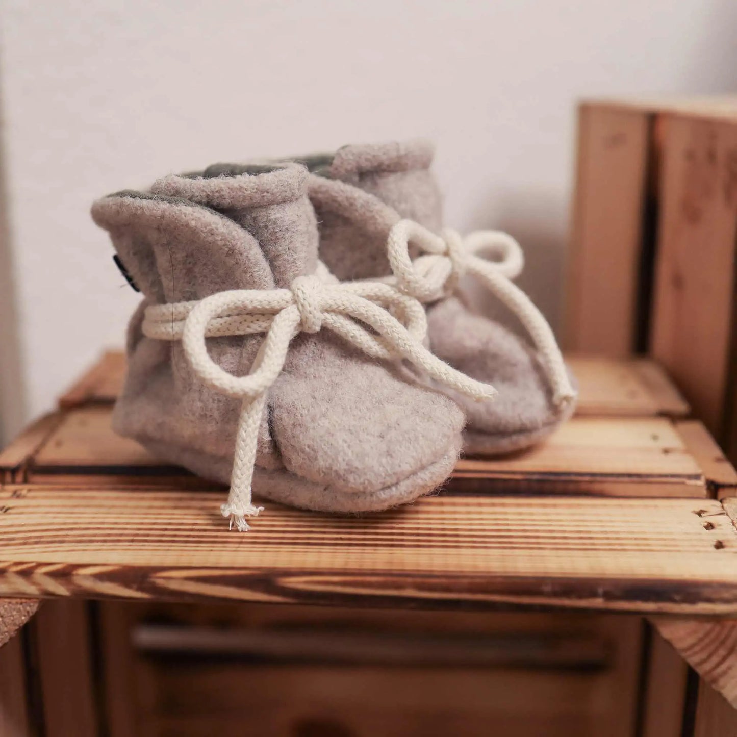 Babyschühchen aus Wollwalk in ecru on a wooden surface, warm wool booties for babies.