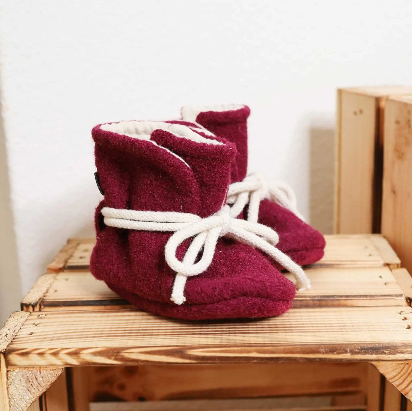 Babyschühchen aus Wollwalk in Bordeauxfarbe auf Holzregal, bietet warme Füßchen für Babys.