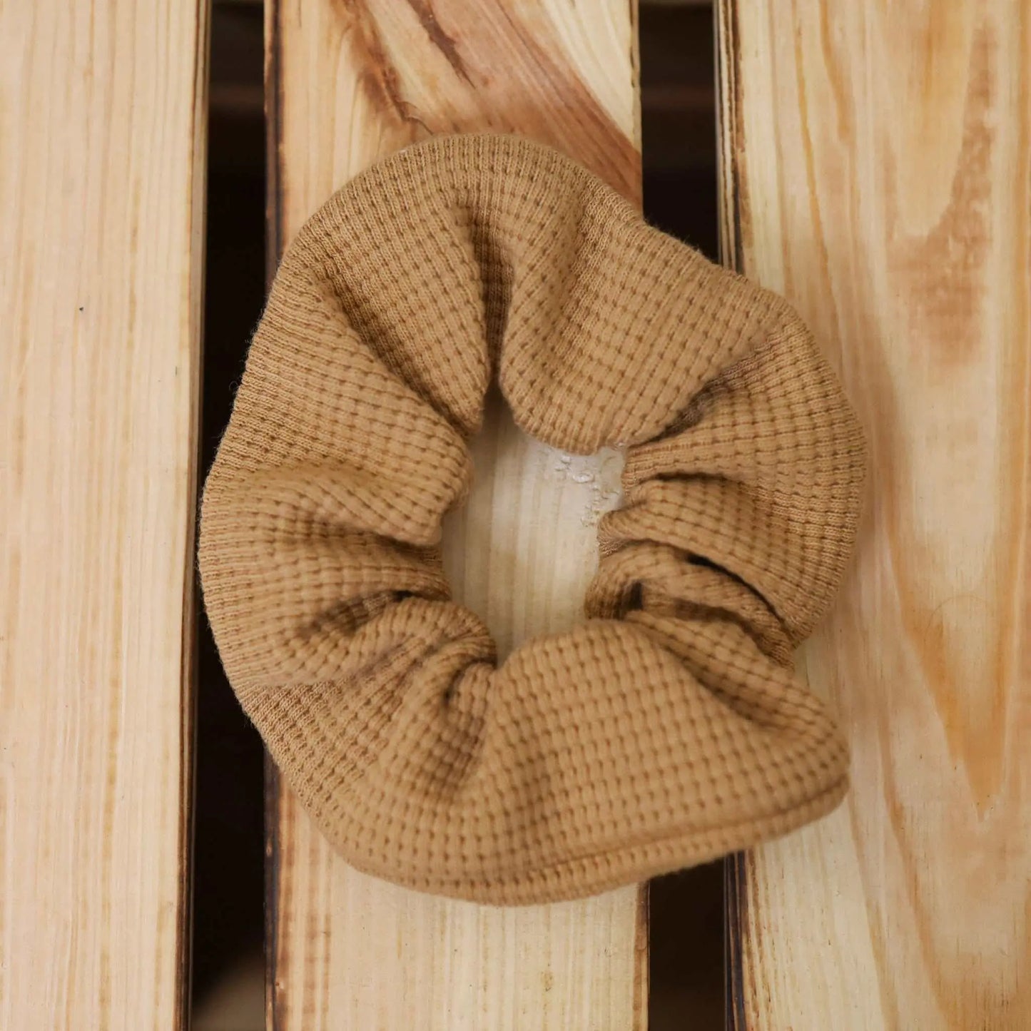 Camel-colored scrunchie made from jersey waffle fabric on a wooden surface.