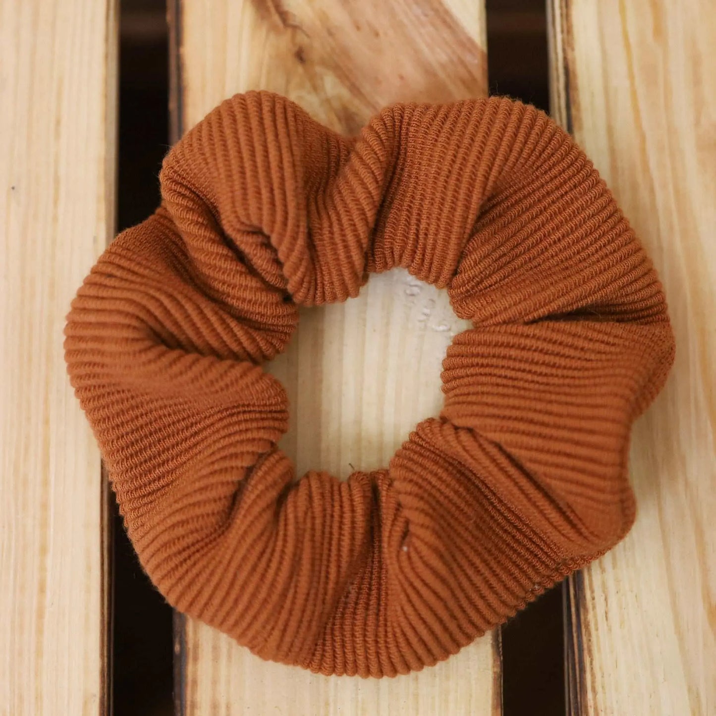 Scrunchie in cognac made from jersey rib fabric, placed on a wooden surface.