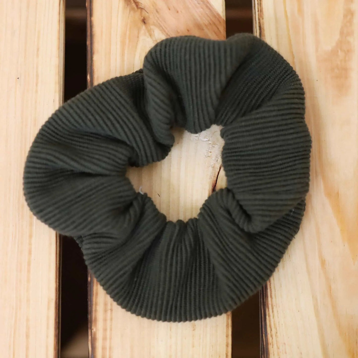 Scrunchie in army green made from jersey rib material, shown on a wooden surface.