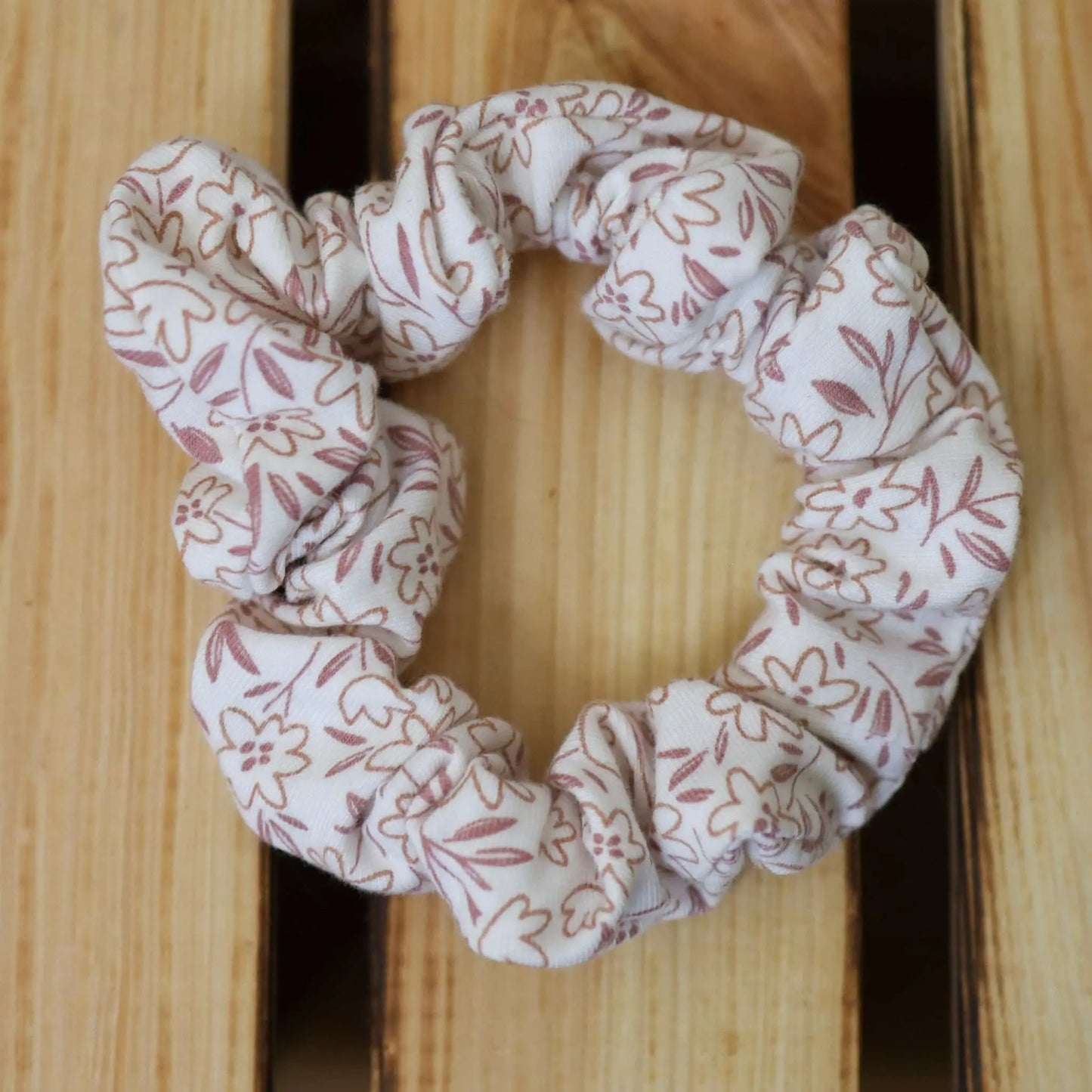 Scrunchie schmal with pink floral design on wooden surface.