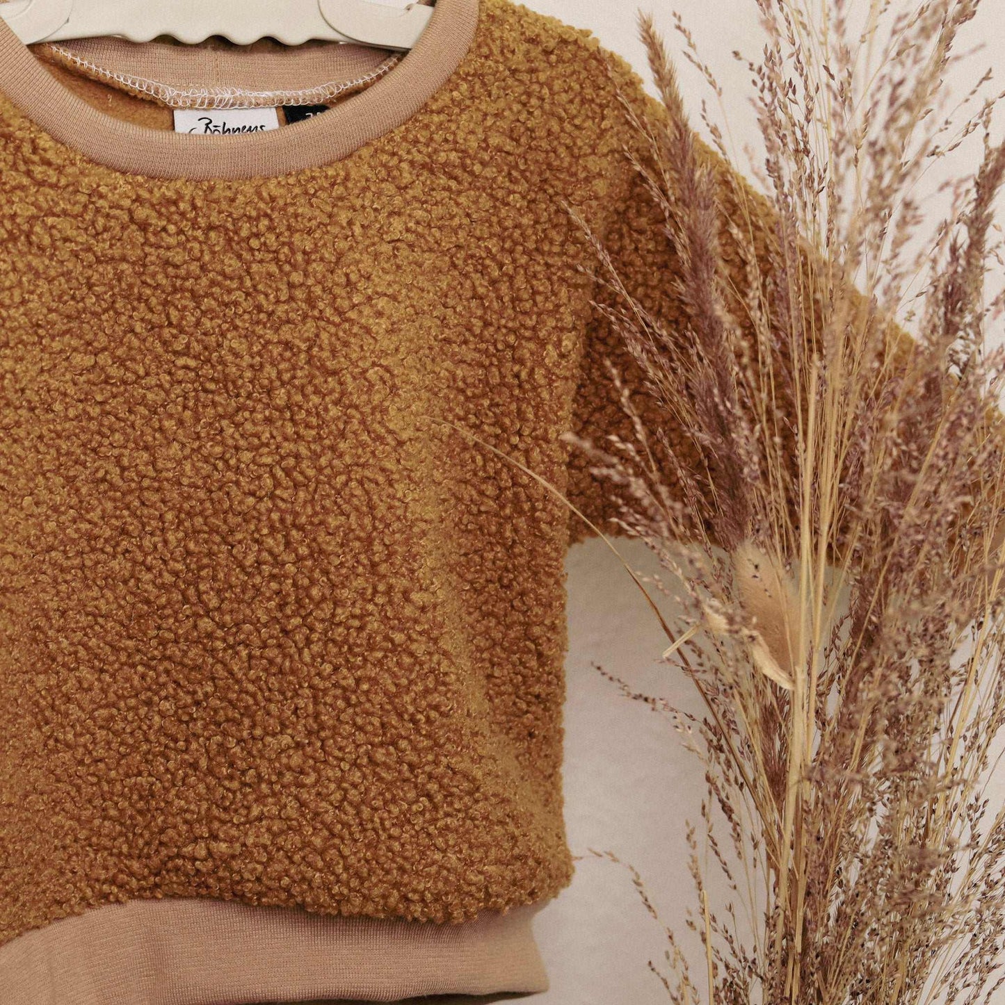 Children's brown teddy fabric Kuschelsweater hanging with decorative dried plants.