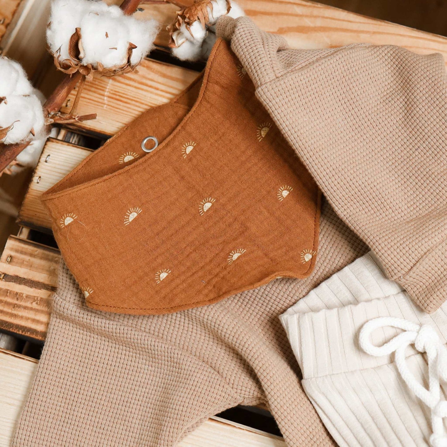 Baby drool bib in rainbow pattern on clothing set, made of absorbent muslin fabric.