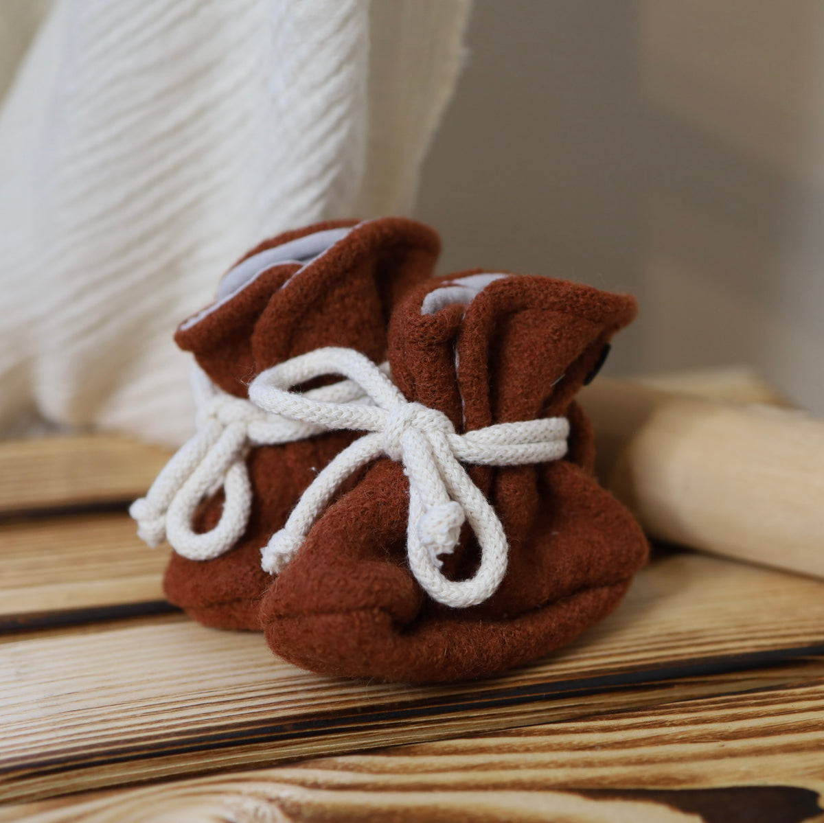 Handgenähte Babyschuhe aus rostrotfarbenem Wollwalk mit cremeweissen Bindebändern